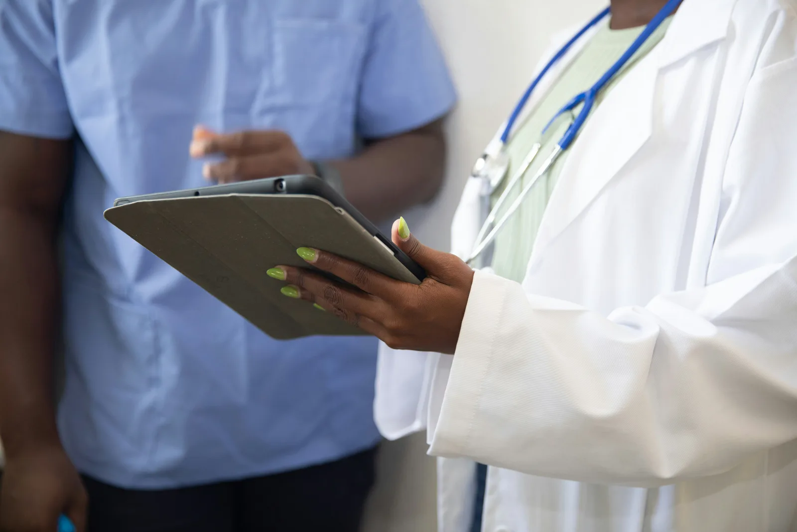 A doctor in a white coat showing results on a tablet to a patient